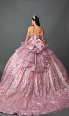 A woman, seen from behind against a gray background, wears the Quinceanera Dress 5169 By Dancing Queen—an off-shoulder, sparkling pink ballgown featuring a full skirt, oversized bow, and tiara.