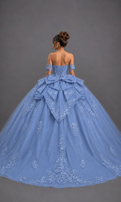 A woman stands against a plain gray background, wearing the Quinceanera Dress 5171 by Dancing Queen—a dazzling blue off-the-shoulder ballgown adorned with elegant floral embroidery, a large bow at the back, and glitter tulle that lends sparkling glamour to the classic silhouette.