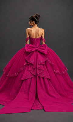 A woman stands facing away against a dark background, wearing the Quinceanera Dress 5172 By Dancing Queen—a magenta ball gown featuring a corset-style bodice, off-the-shoulder sleeves, layered skirt, and a large bow.