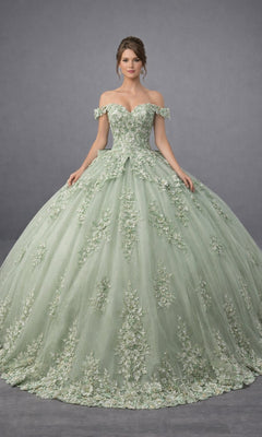 A woman wearing the Quinceanera Dress 5184 By Dancing Queen in sage, featuring an off-shoulder neckline, delicate floral embroidery, and stunning floral appliques on a voluminous ballgown skirt, stands against a plain gray background.