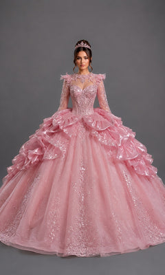 A woman stands against a plain gray background wearing the Quinceanera Dress 5189 By Dancing Queen in pink, featuring a voluminous silhouette with lace details, an embellished fitted bodice, long sheer sleeves, and a matching tiara.