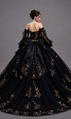 A person wearing the Quinceanera Dress 5190 By Dancing Queen—an off-shoulder black ballgown adorned with intricate gold leaf appliques, featuring a large bow on the back and paired with a tiara—stands against a plain gray background, creating a stunning and unforgettable look for any Quinceanera celebration.