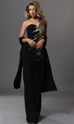 A woman stands against a plain gray background, wearing the Jovani 51900 long formal dress—a fitted black sheath silhouette with a strapless neckline, embellished with gold sequin embroidery—and a matching black shawl.