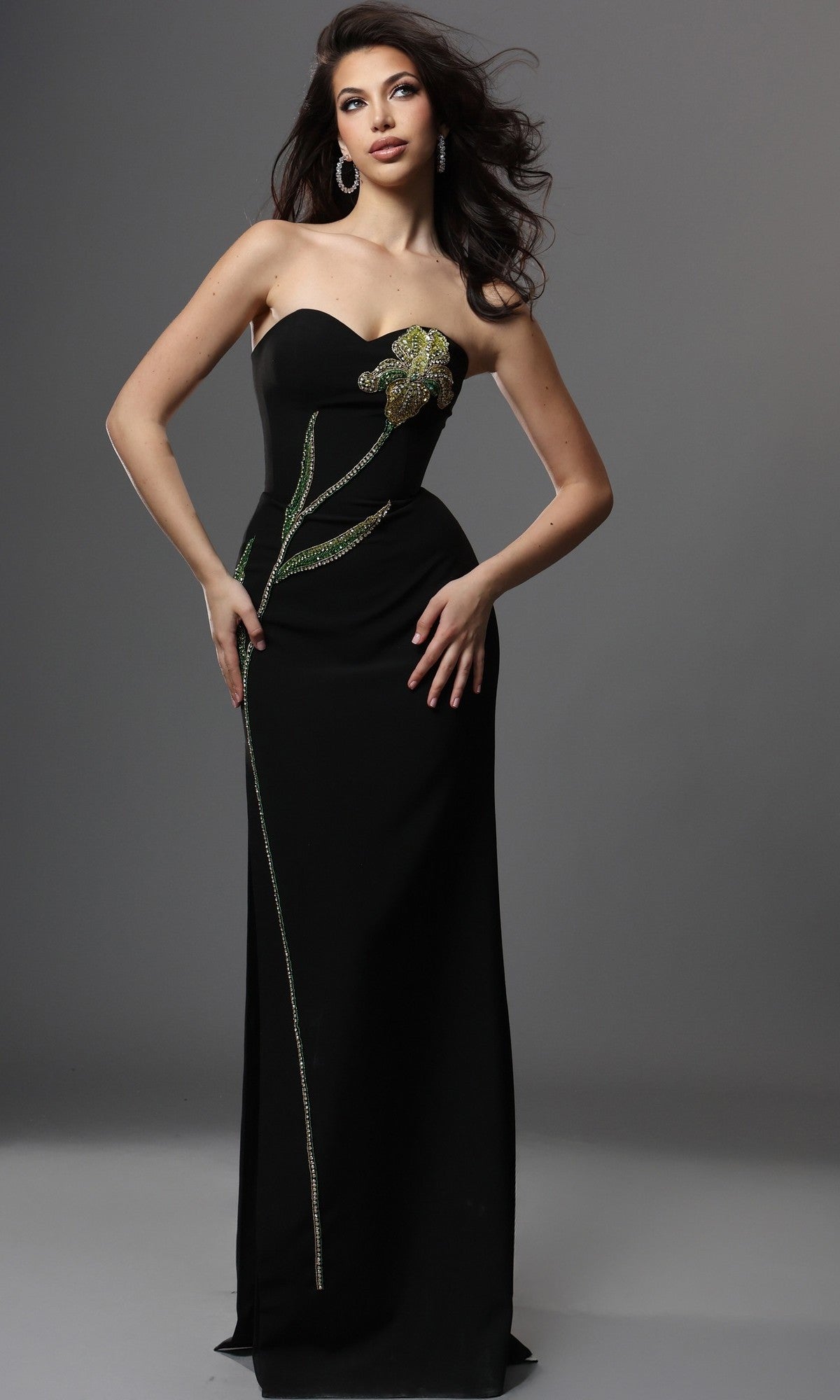 A woman poses in the elegant Jovani 51902 Long Formal Dress, a black strapless gown featuring exquisite beaded embellishments in a sophisticated flower and stem pattern, set against a plain gray background.