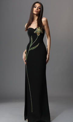 A woman wearing the Jovani 51902 long formal dress—a black, strapless gown adorned with a green and yellow floral design and delicate beaded embellishments—stands against a plain gray background.