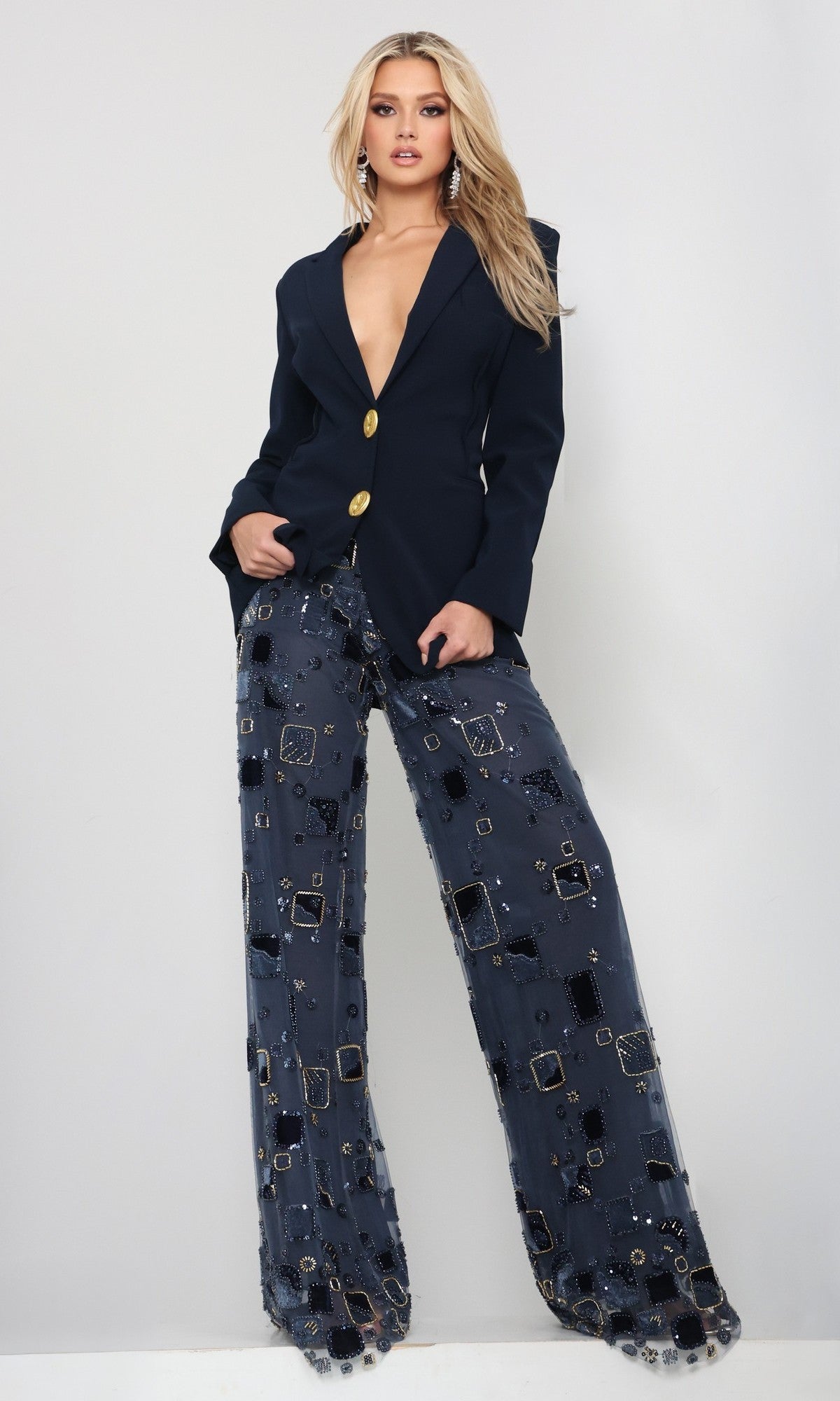 A woman stands against a plain background, wearing the Jovani 52096 long formal jumpsuit in navy.