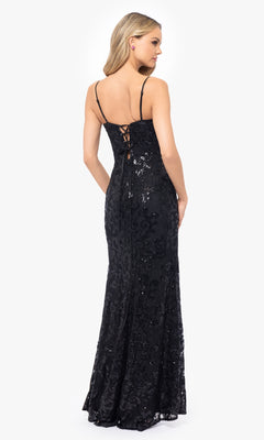 A woman stands facing away in the Blondie Nites 5213BN Black Sequin-Print Prom Dress, featuring a floor-length design with thin straps, a sheer corset bodice, and a lace-up back.