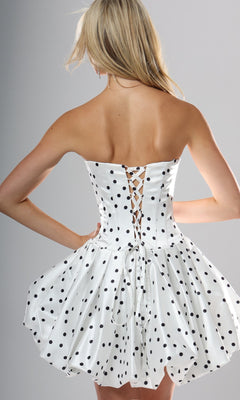 Wearing the Jovani 52165 short homecoming dress, a woman stands out in style with its strapless polka-dot design featuring bold black spots. The fitted corset-style back showcases elegant lace-up detailing, while the flared skirt creates a flattering fit-and-flare silhouette.
