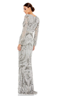 A woman stands against a white background, looking over her shoulder in the Long Formal Dress 5222 by Mac Duggal, featuring silver beading, long sleeves, and a fitted waist.