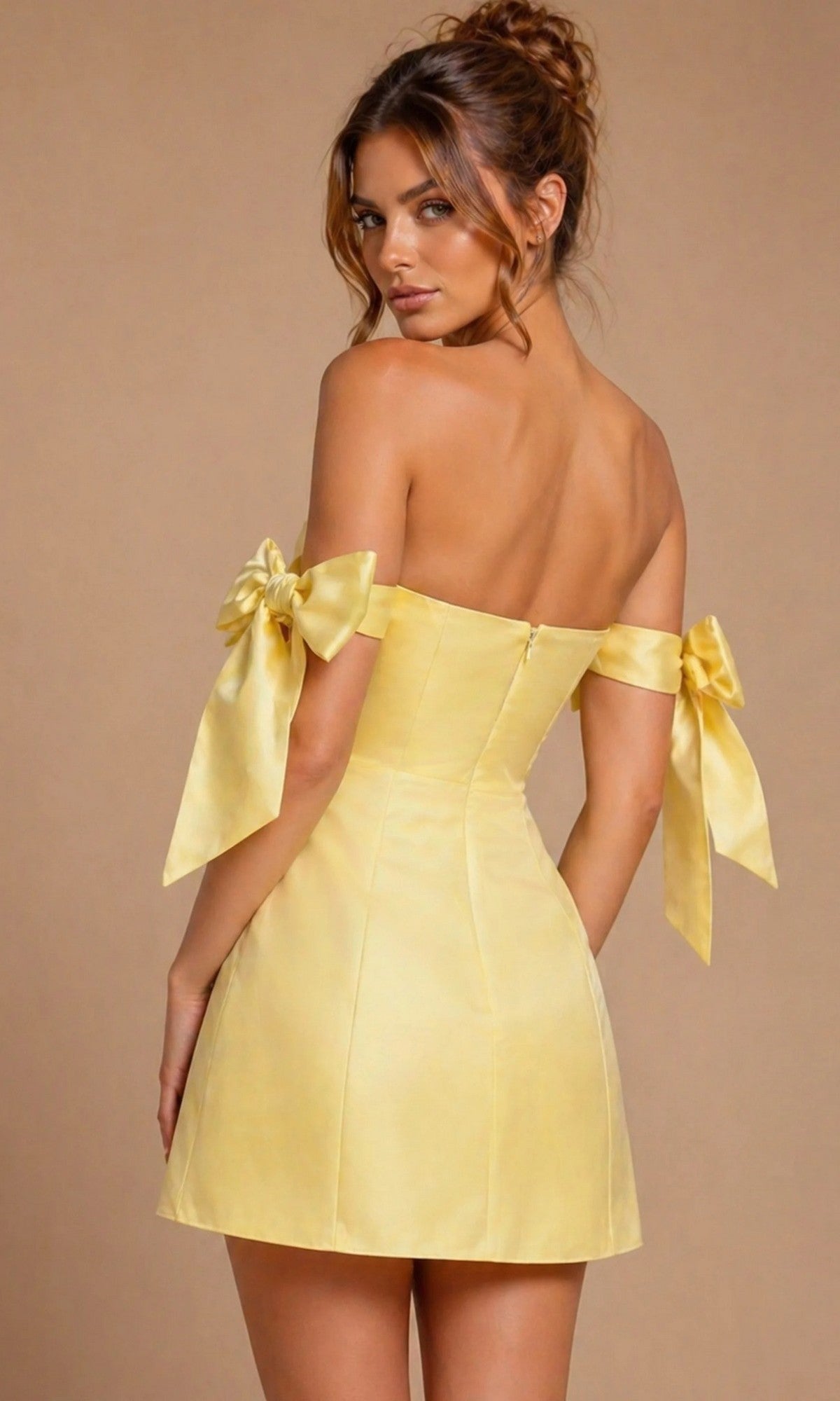 A woman stands facing away, looking over her shoulder, wearing the Jovani 52367 short homecoming dress—a yellow satin mini dress with off-shoulder sleeves adorned with large bow details.