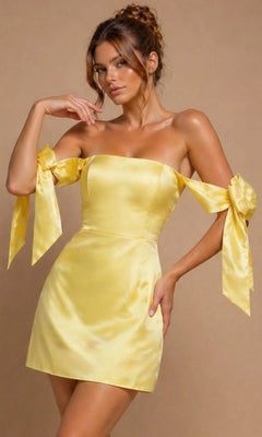 A woman wearing the Jovani 52367 short yellow satin homecoming dress with off-shoulder bow sleeves, standing against a plain beige background.