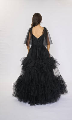 A woman is photographed from the back against a white background wearing the Nina Canacci 5315 long formal dress, featuring black ruffle-tiered tulle and short sheer sleeves.