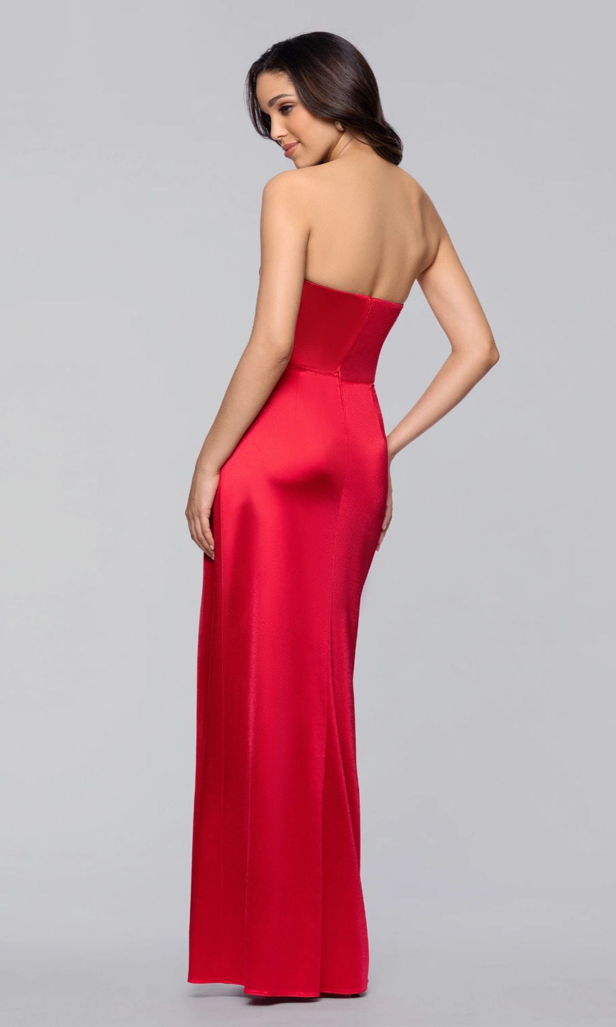 A woman stands against a plain gray background, looking over her shoulder while wearing the Blondie Nites 5355BN long strapless satin prom dress with a sweetheart neckline and floor-length red gown.