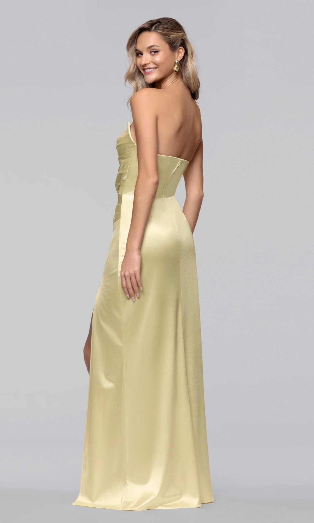 A woman models the Blondie Nites 5355BN long prom dress, featuring a strapless satin design with a sweetheart neckline, as she stands smiling over her shoulder against a plain light gray background.