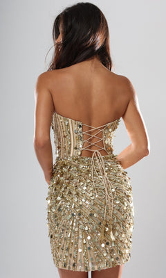 Wearing the Jovani 53770 Short Homecoming Dress, a woman is seen from behind against a plain light background. The dress features a strapless sequin design with a lace-up open back and corset bodice detail.