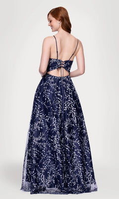 A woman models the Blondie Nites 5386BN long prom dress—navy blue, floor-length with an A-line skirt, silver floral glitter print, open back, and thin straps—against a plain light background.