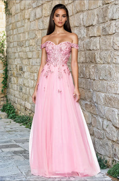 A woman stands outdoors by a stone wall, wearing the Blondie Nites 5389BN blush pink prom dress featuring a sweetheart corset bodice, beaded floral lace embroidery, and a flowing tulle skirt.