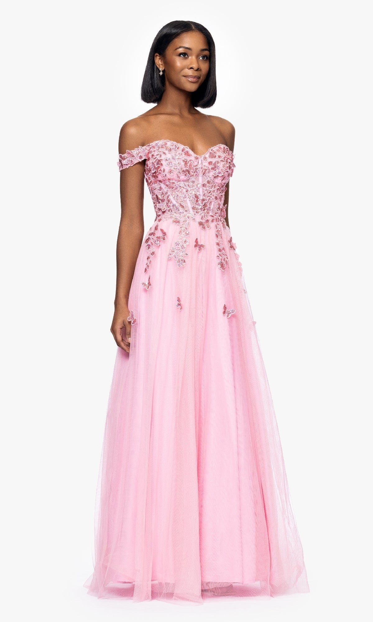 A woman in the Blondie Nites 5389BN blush pink prom dress with a sweetheart corset bodice and floral embellishments stands against a plain white background.
