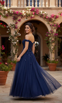 A woman in the Blush Pink Prom Dress: Blondie Nites 5389BN stands outdoors, looking back and smiling. Flowering vines and arched columns appear in the background.