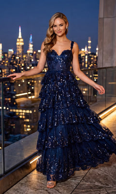 A woman wears the Blondie Nites 5394BN Beaded-Lace Ruffle Prom Gown, featuring ruffled tiers and a corset-style bodice, as she stands on a balcony at night overlooking a sparkling city skyline.