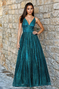 A woman stands against a stone wall wearing the Blondie Nites 5406BN, a teal long glitter A-line prom dress with a deep V-neckline.