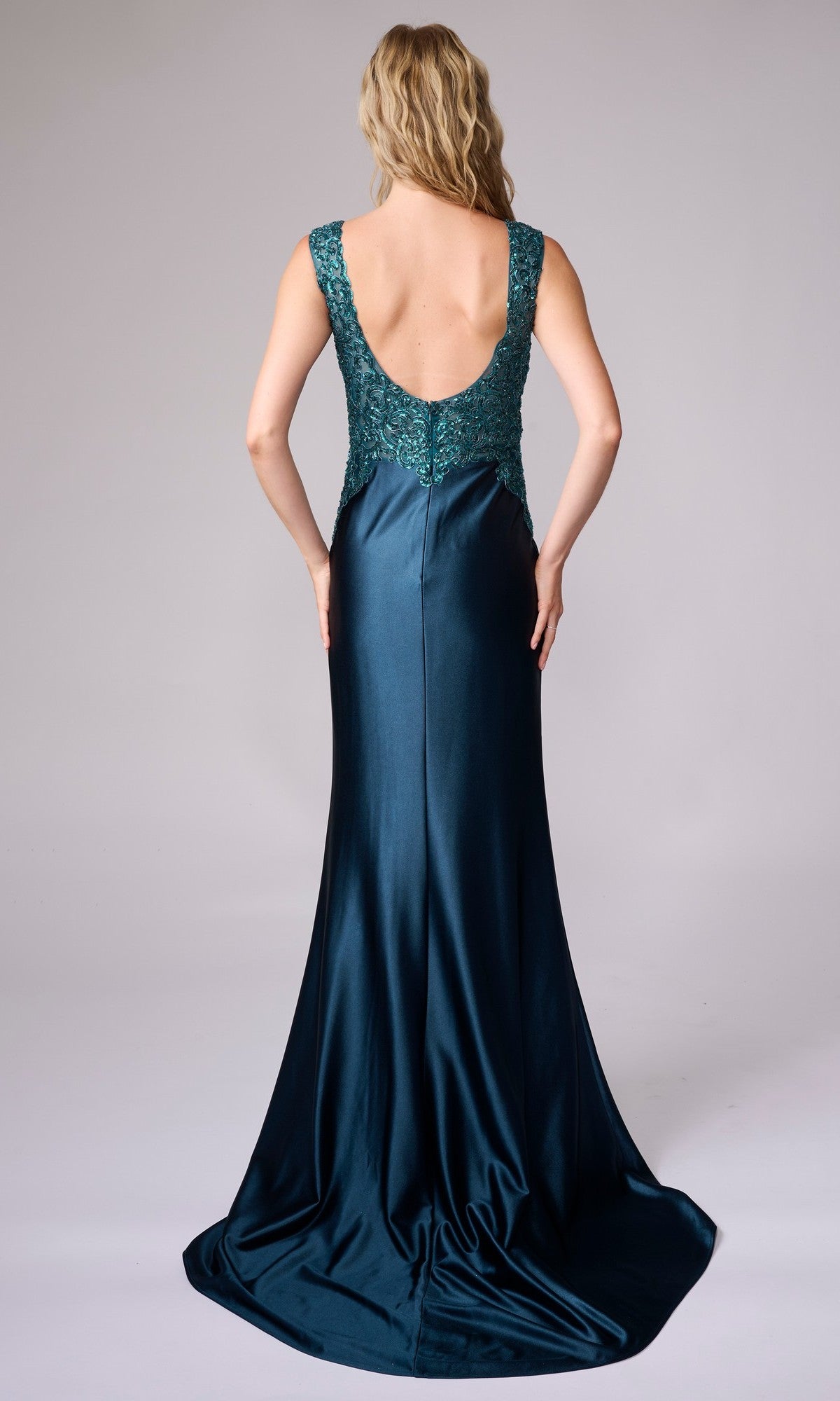 A woman faces away in the Nina Canacci 5411, a dark teal sleeveless formal gown that's floor-length with a low back and an embellished lace-detailed bodice.