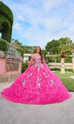 A young woman stands in a garden wearing the Quinceanera Dress 54200 By Amarra—a bright pink, off-the-shoulder gown with delicate floral embroidery, matching gloves, and a sparkling tiara.