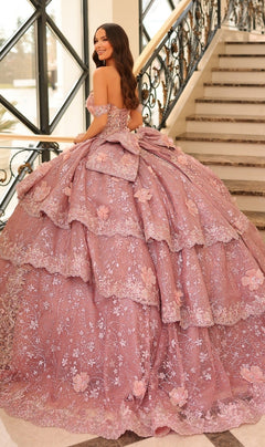 A woman wearing the Quinceanera Dress 54202 by Amarra, a lavish off-the-shoulder ball gown with lace embroidered flowers, stands on a staircase, smiling and looking over her shoulder.