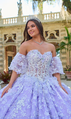 A young woman in the Quinceanera Dress 54206 By Amarra, a lavender ball gown with glow-in-the-dark floral lace and a tiara, stands outdoors before a stone building.