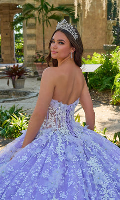 A young woman poses outdoors, looking over her shoulder in the Quinceanera Dress 54206 By Amarra, a ball gown adorned with white floral details and a tiara.