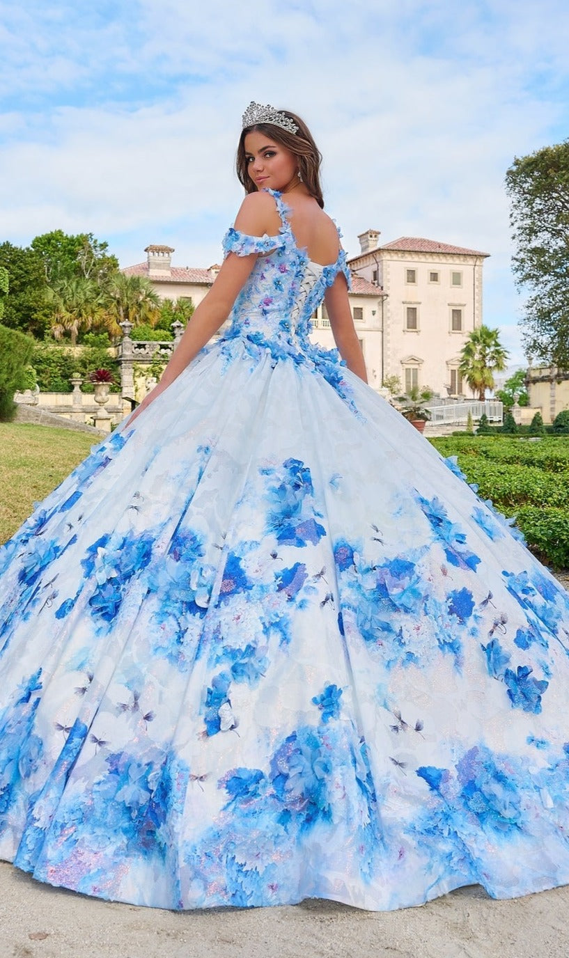 A young woman in the Quinceanera Dress 54208 By Amarra and a tiara stands outdoors before a grand building.