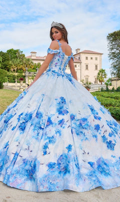 A young woman in the Quinceanera Dress 54208 By Amarra and a tiara stands outdoors before a grand building.