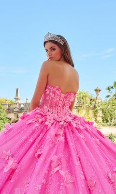 A young woman in the Quinceanera Dress 54218 By Amarra—a strapless, bright pink ball gown with floral details and a tiara—stands outdoors, looking over her shoulder.
