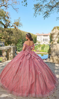 A young woman in the Quinceanera Dress 54226 By Amarra stands outdoors on stone steps, facing away, with a garden and large building behind her.