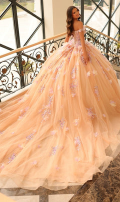 A woman stands on a staircase wearing the Quinceanera Dress 54228 by Amarra, an off-the-shoulder peach ball gown with 3D floral appliqué and a long train, looking back over her shoulder.