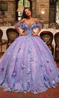 A woman stands indoors wearing the Amarra 54229 Glitter Tulle Quinceañera Dress, a floor-length, off-shoulder lavender ball gown adorned with floral embroidery, delicate beading, and sparkling glitter tulle embellishments.