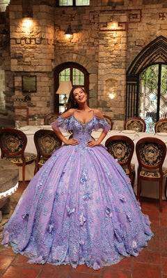 A woman smiles in an ornate stone hall, wearing the Amarra 54229 Glitter Tulle Quinceañera Dress—a detailed lavender ball gown—surrounded by decorative chairs and arched windows.