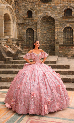 A young woman stands outdoors on stone steps, wearing the Amarra 54229 Glitter Tulle Quinceañera Dress, an elaborate pink ball gown adorned with floral embellishments, beading, and sparkling glitter tulle.