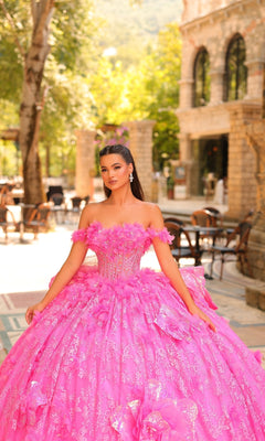 A woman stands outdoors in the Amarra 54233 3D Flower Quinceanera Dress, featuring a voluminous off-the-shoulder ball gown with an embellished bodice. Trees and stone buildings are visible in the background.