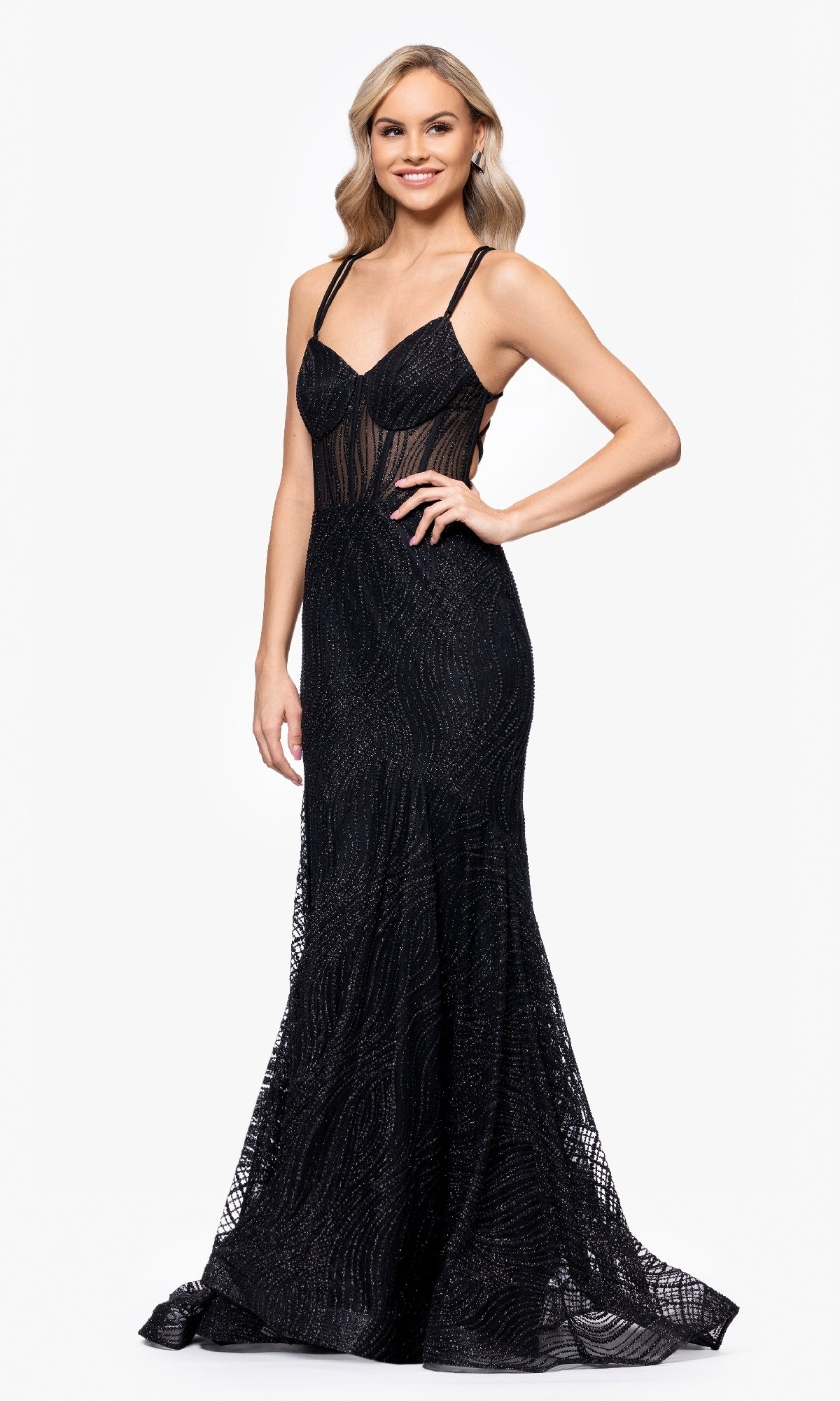 A woman in the Long Prom Dress: Blondie Nites 5426BN, a floor-length black glitter gown with thin straps, shimmering patterns, and a sheer corset bodice, stands smiling against a plain white background.