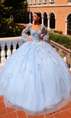 A woman wearing the Corset Ball Gown Quinceañera Dress 59290 by Amarra and a tiara stands on a balcony with Mediterranean-style architecture in the background.