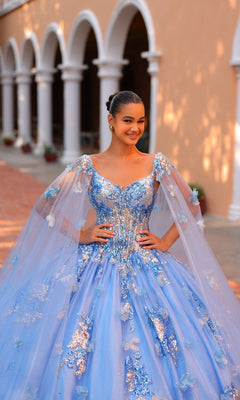 A young woman smiles in front of an arched building, wearing the Quinceanera Dress 54318 by Amarra?a ball gown with floral embroidery and a sheer cape.