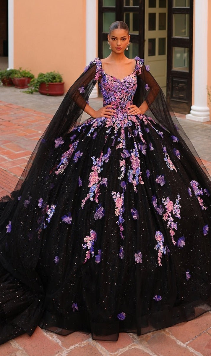 A woman stands outdoors in the Quinceanera Dress 54318 By Amarra, a stunning ball gown adorned with purple and lavender floral appliqu‚s, sheer cape sleeves, and elegant embroidery.