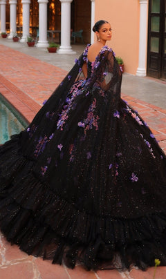 A woman stands by a pool wearing the Quinceanera Dress 54318 By Amarra, a dramatic black ball gown with purple floral embroidery, sheer flowing layers, and a delicate corset bodice.