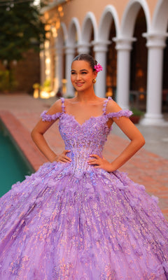 A young woman in the Quinceanera Dress 54320 By Amarra, an off-shoulder lavender ball gown with 3D floral accents, stands by a pool smiling with her hands on her hips and a flower in her hair. Arched columns are visible behind her.