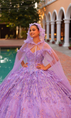 A young woman stands by a pool wearing the Quinceanera Dress 54320 by Amarra, an off-the-shoulder lavender ball gown with a matching cape and hood, featuring beautiful 3D floral details.
