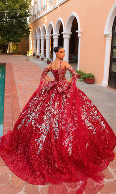 A woman in the Quinceanera Dress 54322 By Amarra stands on a brick pathway beside a pool, with an arched building in the background.
