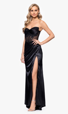A woman models the Blondie Nites 5434BN strapless black prom dress with a sheer bodice and side slit, paired with high heels, standing against a plain white background.