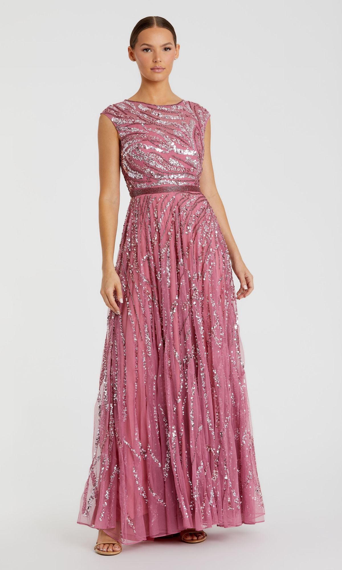 A woman wears the Mac Duggal 5445 High-Neck Beaded Formal Gown, a sleeveless, floor-length pink dress with silver sequin patterns, fitted bodice, and flared skirt.
