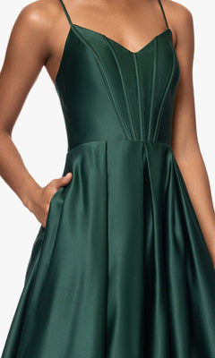 A person wears the Blondie Nites 5446BN Classic Long Prom Dress, a sleeveless dark green satin A-line gown with thin straps, a fitted V-neck corset bodice, and side pockets.